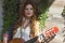 A beautiful girl with red curly hair stands and holds a seven-string guitar in her hands.