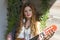 A beautiful girl with red curly hair stands and holds a seven-string guitar in her hands.