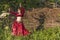 Beautiful girl in red dress dances incendiary dance on summer meadow against of hedge.