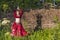 Beautiful girl in red dress dances incendiary dance on summer meadow against of hedge.