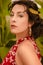 A beautiful girl in a red dress and with earrings in the rings in the greenhouse. Woman in Spanish style on a background of green