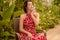 A beautiful girl in a red dress and with earrings in the rings in the greenhouse. Woman in Spanish style on a background of green