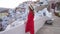 Beautiful girl in red dress and hat climbs the stairs exploring Oia village, Santorini, Greece