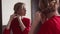 Beautiful Girl in Red Dress Looking in the Mirror - Portrait of a young woman in a room wearing party gown.