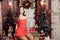 Beautiful girl in red mini dress sits on Christmas decorations background. New Year`s street festive decor