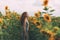 Beautiful girl with red wavy hair and freckles in stripped colourful dress enjoying nature on the field of sunflowers.