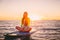 Beautiful girl relaxing on stand up paddle board, on a quiet sea with warm sunset colors.