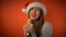 beautiful girl in Santa Claus hat smiles and sings into karaoke microphone on red background. Celebrating new year 2022