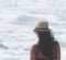 Beautiful girl, seen from behind, with hat who look the sea. Sea in the background.