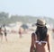 Beautiful girl, seen from behind, with hat who walk on the beach. People in the background.