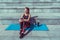 Beautiful girl sits mat, fitness summer city, outdoors, yoga after workout, relaxation, enjoyment of pleasure music with