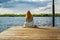 A beautiful girl is sitting alone on the river pier against the backdrop of thunder clouds and looks into the distance.