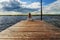 A beautiful girl is sitting alone on the river pier against the backdrop of thunder clouds and looks into the distance.