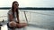 Beautiful girl sitting on deck of boat and looking to nature on sunny day.