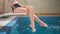 beautiful girl is sitting on diving board for pool and wetting her feet in beautiful transparent blue water while