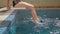 beautiful girl is sitting on diving board for pool and wetting her feet in beautiful transparent blue water while