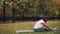 Beautiful girl in sportswear is exercising in park practising seated twists and forward bends on yoga mat on warm autumn