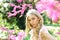 Beautiful girl standing under gentle tree with tiny hot pink blossom. Elegant young lady with long, blond, curled hair