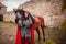 A beautiful girl stands next to a horse against the background of a medieval fortress. Fantasy costume, chain mail, cloak. A woman