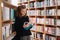 Beautiful girl is studying reading a book while standing on the floor among books in the bookshop