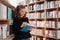 Beautiful girl is studying reading a book while standing on the floor among books in the bookshop