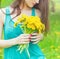 Beautiful girl in a Sunny summer day walking in the garden and keeps yellow dandelions in the hands