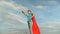 Beautiful girl superhero standing on field in red cloak, cloak fluttering in wind. Slow motion. close-up. girl dreams of