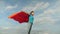 Beautiful girl superhero standing on the field in a red cloak, cloak fluttering in the wind. Slow motion. girl dreams of