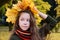 beautiful girl in sweater and scarf with wreath of yellow maple leaves on her head. Teenage girl walks through autumn park