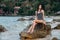 Beautiful girl in a swimsuit posing on rocks in the sea. Against the background of hotels bungalows.