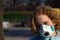 Beautiful girl tilted her head and looking at the camera. Respiratory protective medical mask. Health protection concept. Outdoor