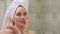 Beautiful girl with a towel on her head puts cream on her face in the bathroom