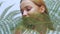 Beautiful girl in tropical leaves in the studio touches her face, the concept of natural cosmetics. Blonde looking at camera