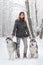 The beautiful girl with two dogs huskies poses in beautiful for the snow wood. Trees in snow