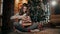 A beautiful girl is unwrapping a christmas present sitting on the floor in a well-decorated living room.