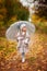 Beautiful girl in vintage outfit with a transparent umbrella walks in autumn park, orange background