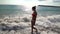Beautiful girl walking barefoot along sand beach beside sea shallows.