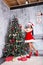 Beautiful girl wearing santa claus clothes . Young woman decorating Christmas tree with red balls at home