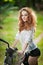 Beautiful girl wearing white lace blouse and black shorts having fun in park with bicycle. Pretty red hair woman posing