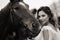 Beautiful girl in a white sundress next to a horse on an old ranch. black and white photo