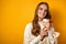 Beautiful girl in a white sweater smiling is standing on a yellow background and holding a thermomug in her hands.