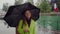 Beautiful girl in a yellow coat stands in the rain, twists a cute black umbrella, smiles and flirts. Lake Annecy, France