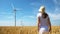 Beautiful girl on yellow field of wheat with windmills for electric power production