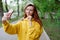 A beautiful girl in a yellow hoodie takes a selfie, holds her phone in her hands and adjusts her hair