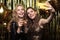 Beautiful girlfriends in high spirits take selfie at party on gold background