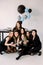 Beautiful girls in black celebrating birthday sitting on the floor. Decorated table with air balloons, cake, drinks and
