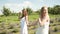 Beautiful girls holding hands in white dresses and long hair walking on a lavender field. Brunette and blonde Caucasian