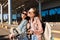 Beautiful girls in sunglasses happily taking photo on cellphone together with backpack on shoulder near airport