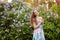 Beautiful glamour girl with long wavy hair and beautiful make-up , in a bright dress stands near a Bush of lilacs in summer and l