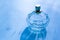 Beautiful glassy faceted bottle with flowery aromatic toilet water eau de perfume on blue background.